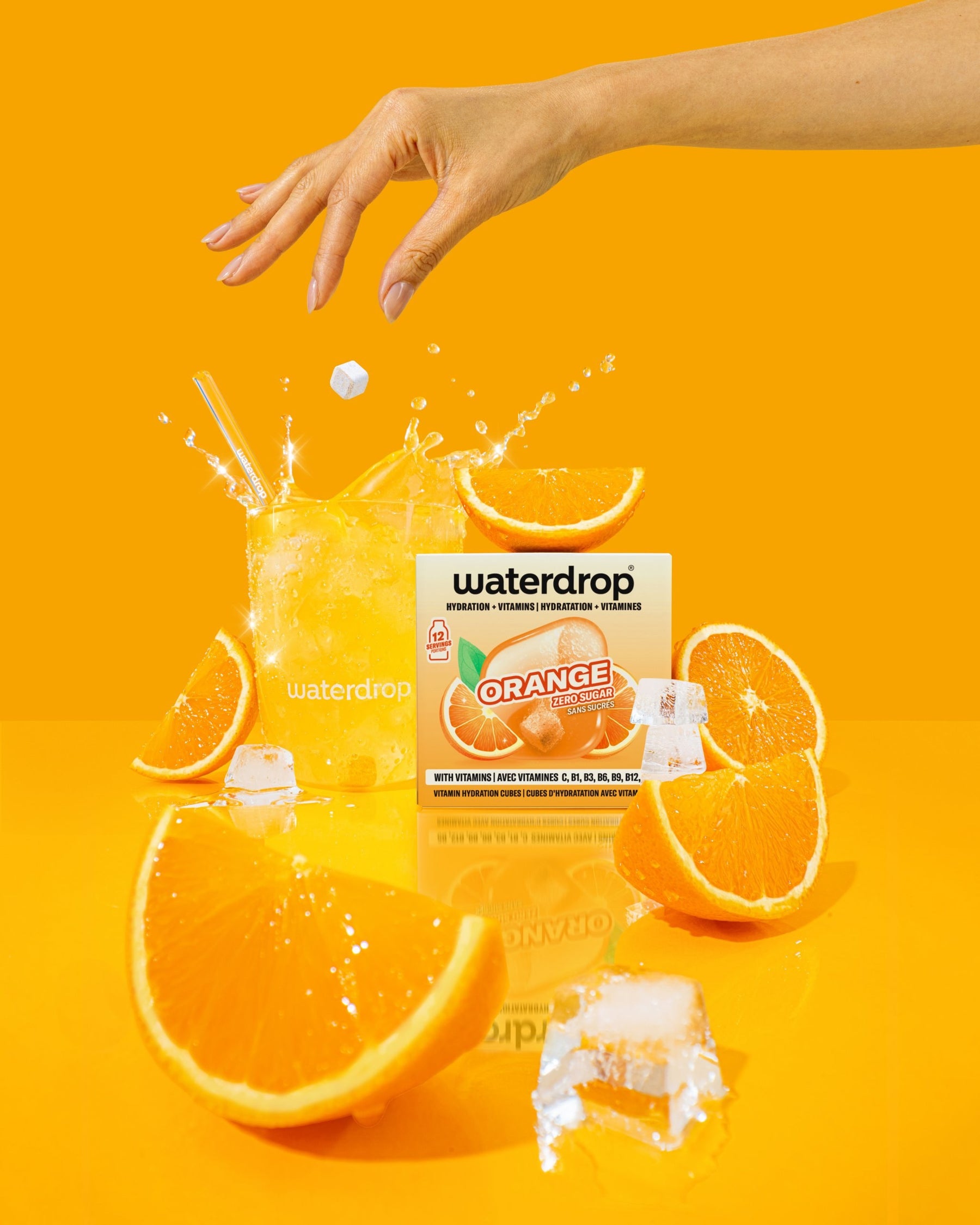 オレンジ味のWaterdropの箱とオレンジのスライス、氷の塊が鮮やかなオレンジ色の背景に置かれています。